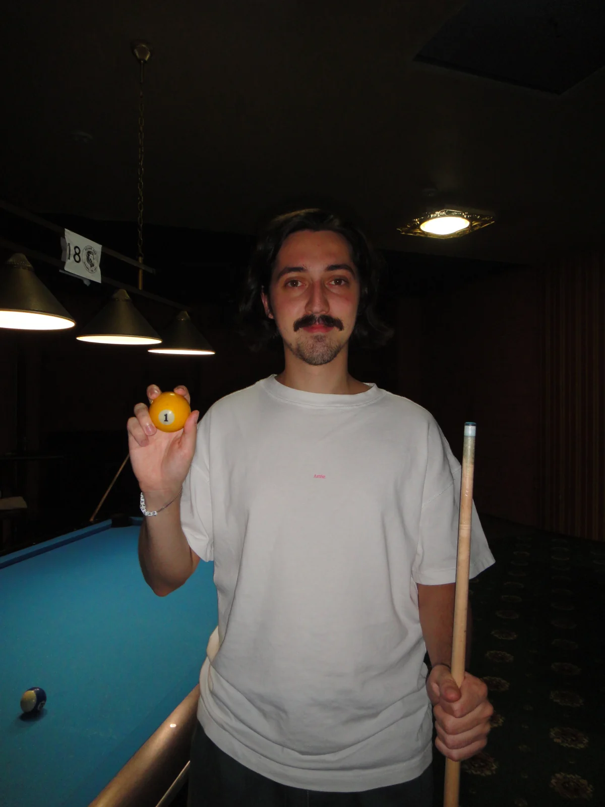 Vlad Duhnov holding the number one pool ball beside a pool table